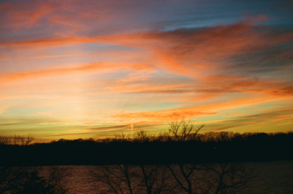 a sunset over a body of water with trees in the foreground