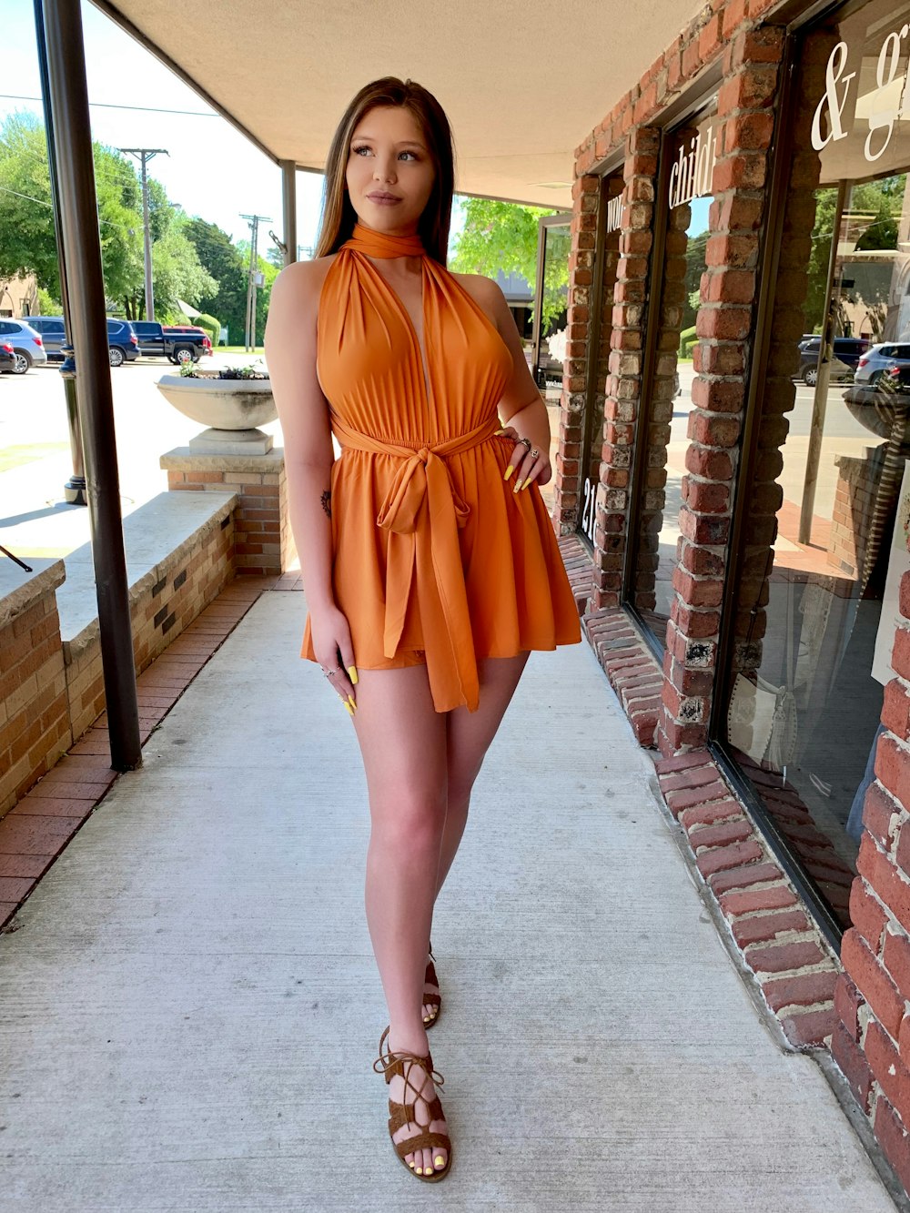 a woman in an orange dress standing on a sidewalk