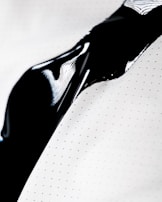 A close-up view of a smooth and shiny black liquid flowing over a white surface with small polka dots. The liquid creates a glossy texture with reflections of light.