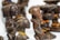 Several intricately carved wooden sculptures are displayed, featuring elongated faces and stylized bodies. The sculptures have a dark, polished finish, some adorned with colorful beaded necklaces. The craftsmanship reflects traditional art styles.