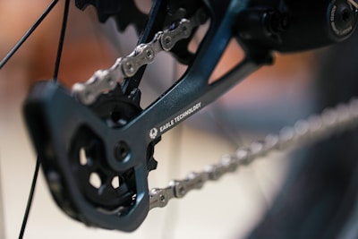 A close-up view of a bicycle drivetrain featuring a chain and rear derailleur with the words 'Eagle Technology' visible on the component. The focus is on the intricate details of the chain and gear mechanism.