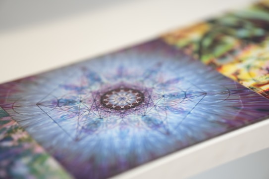 A close-up of a piece of abstract digital art featuring a kaleidoscopic geometric pattern. The intricate design is centered with lines radiating outward in varying shades of blue and purple. The details suggest a combination of symmetry and complexity, giving a sense of movement and depth.