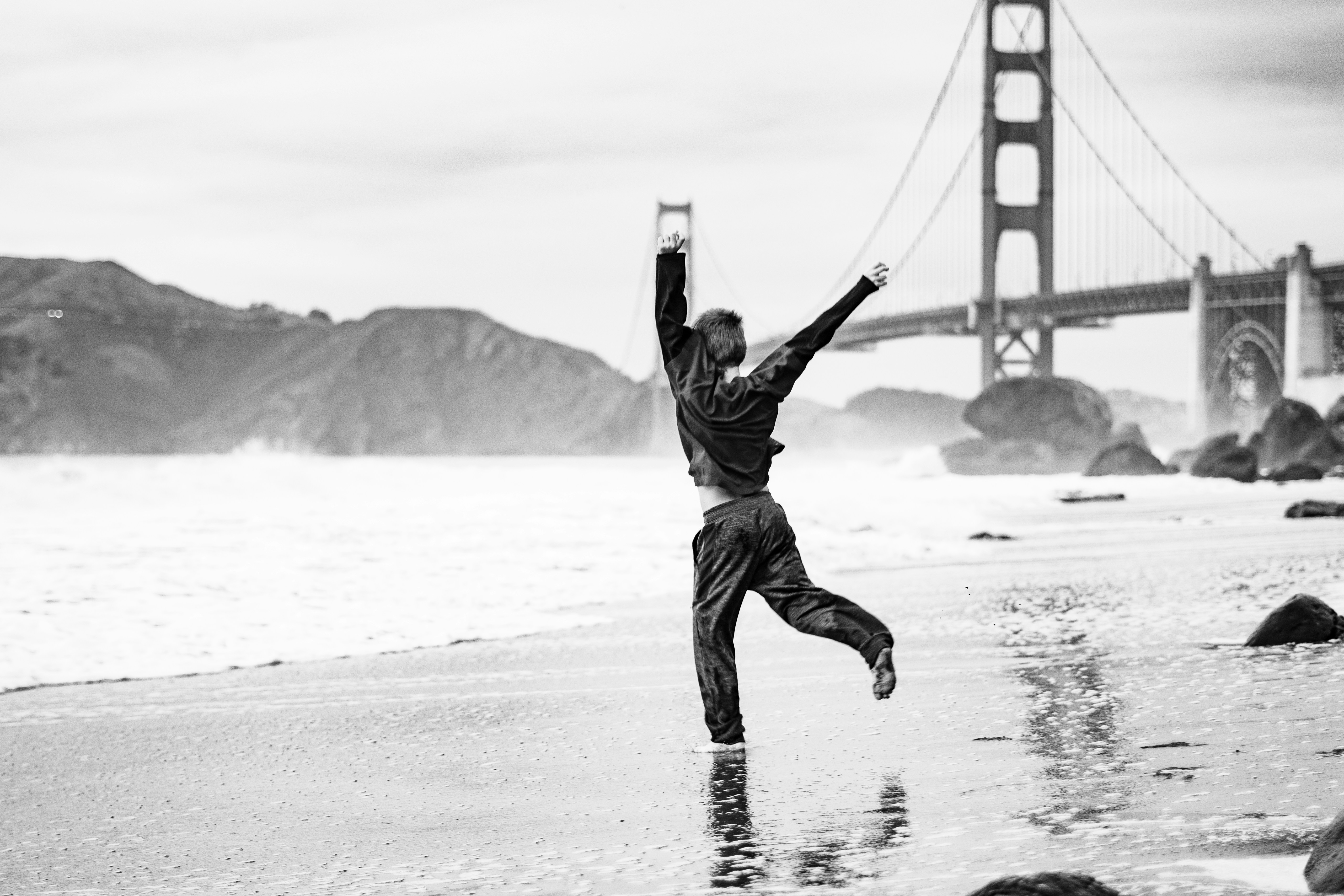 a man standing on a beach in front of a bridge