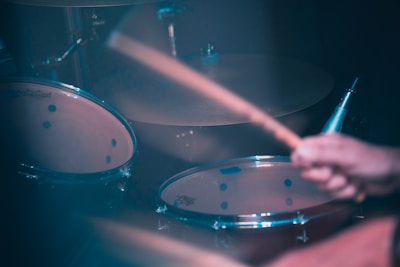 A close-up of a drum set being actively played, with drumsticks in motion and a blurred background giving a sense of movement.