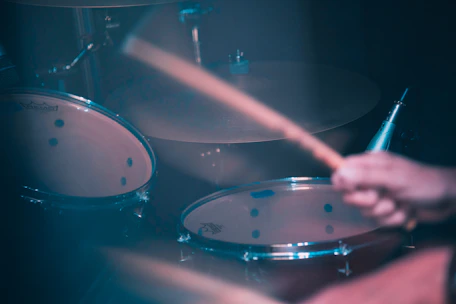 A close-up of a drum set being actively played, with drumsticks in motion and a blurred background giving a sense of movement.
