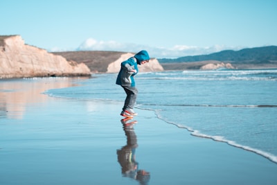 A child laughing in a lightweight hoodie playing near tide pools filled with colorful sea life.