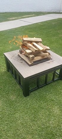 A neatly arranged fire pit with wood bundles and accessories on a wooden deck.