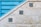 A textured stone wall features three decorative blue tiles arranged diagonally along its surface. Adjacent to the wall is a blue metallic structure with horizontal slats, creating a geometric contrast with the stone. The tiles display intricate floral patterns in shades of blue and green.