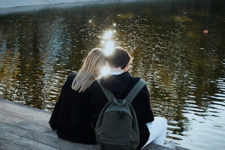 two people sitting on a dock looking at the water