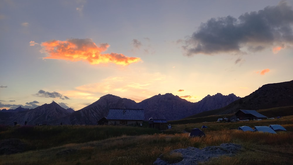 El sol se está poniendo sobre las montañas con una casa en primer plano