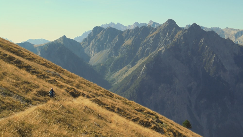 uma pessoa subindo uma colina gramada com montanhas ao fundo