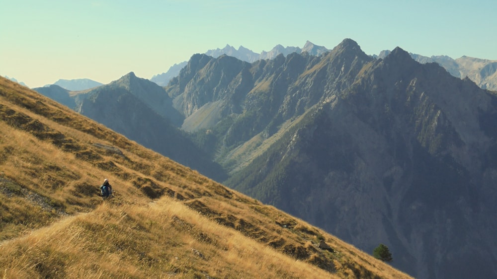 a person walking up a grassy hill with mountains in the background