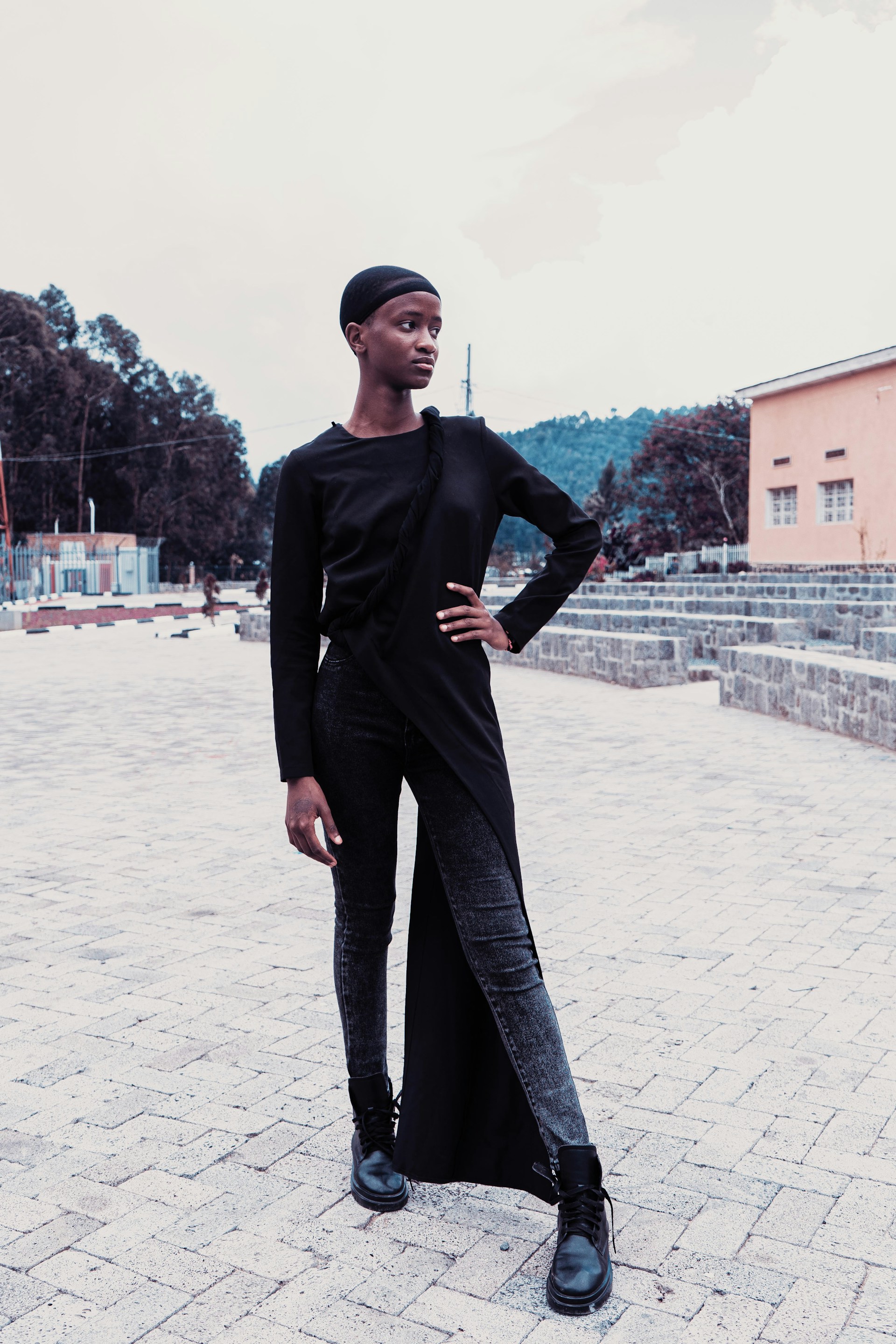 A candid street-style photo of a person wearing a flowing unisex trench coat paired with sleek black boots, walking confidently on a muted city sidewalk.