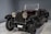 A vintage car with large round headlights, a dark sleek body, and a convertible top. The vehicle is parked indoors on a marble floor and has classic design elements with a visible spare tire attached to the side.