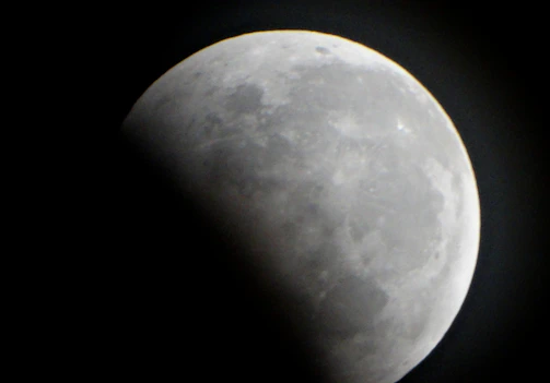 A close-up of a dark moon’s cratered surface under a faint aurora.