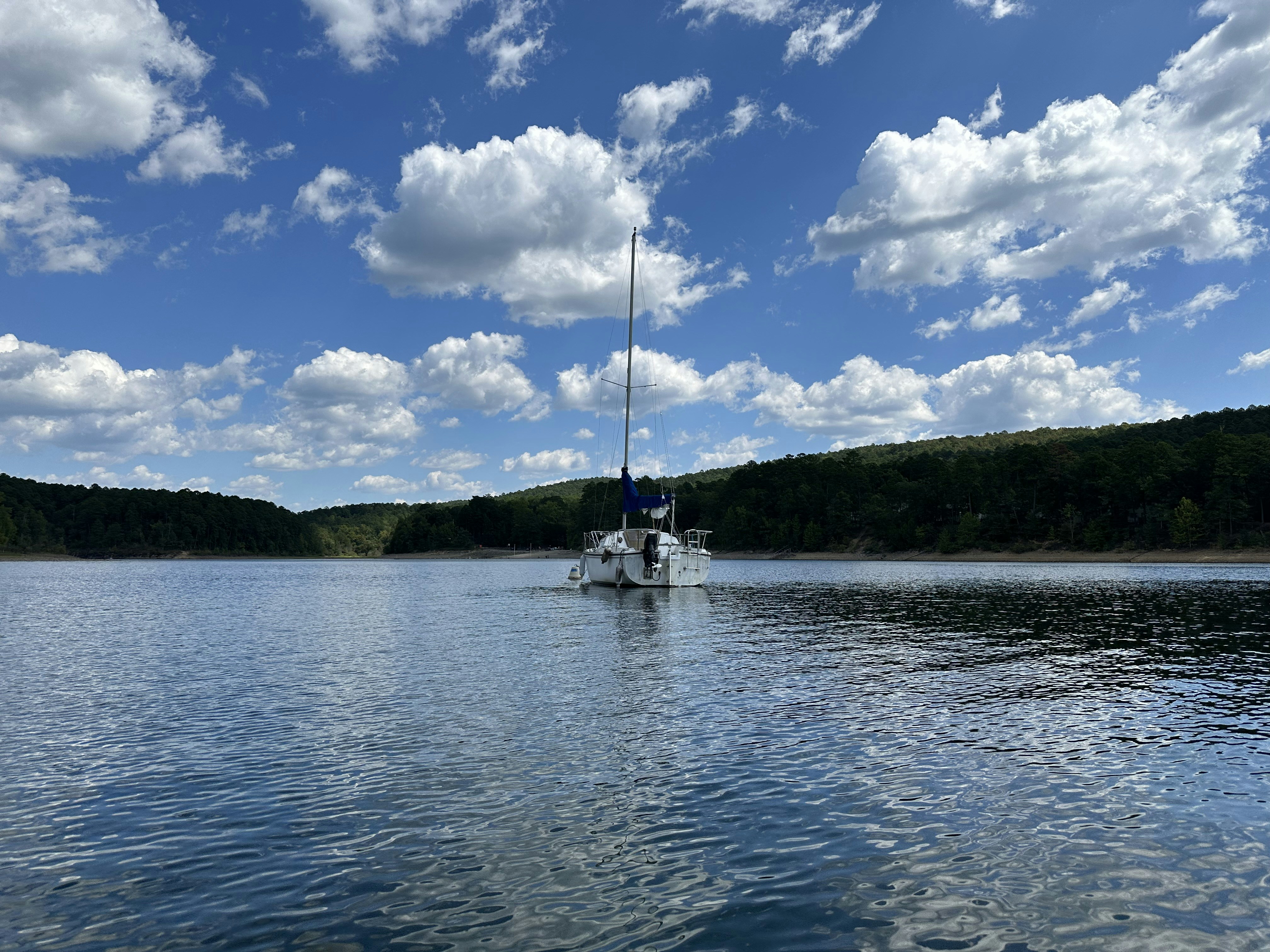 a boat floating on top of a lake under a cloudy blue sky, 