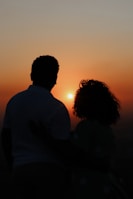 Silhouette of two people embracing tenderly against a sunset backdrop.