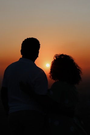 Silhouette of two people embracing tenderly against a sunset backdrop.