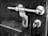 A close-up of a metal door latch against a textured, dark wooden door. The latch is a shiny, chrome-plated bolt style with screws visible on the mounting plates.