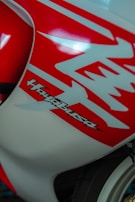 Close-up of a motorcycle's body featuring bold red and white graphics with the word 'Hayabusa' prominently displayed. The design is sleek and aerodynamic, emphasizing speed and style.