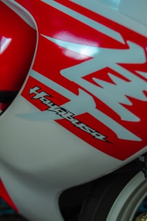 Close-up of a motorcycle's body featuring bold red and white graphics with the word 'Hayabusa' prominently displayed. The design is sleek and aerodynamic, emphasizing speed and style.