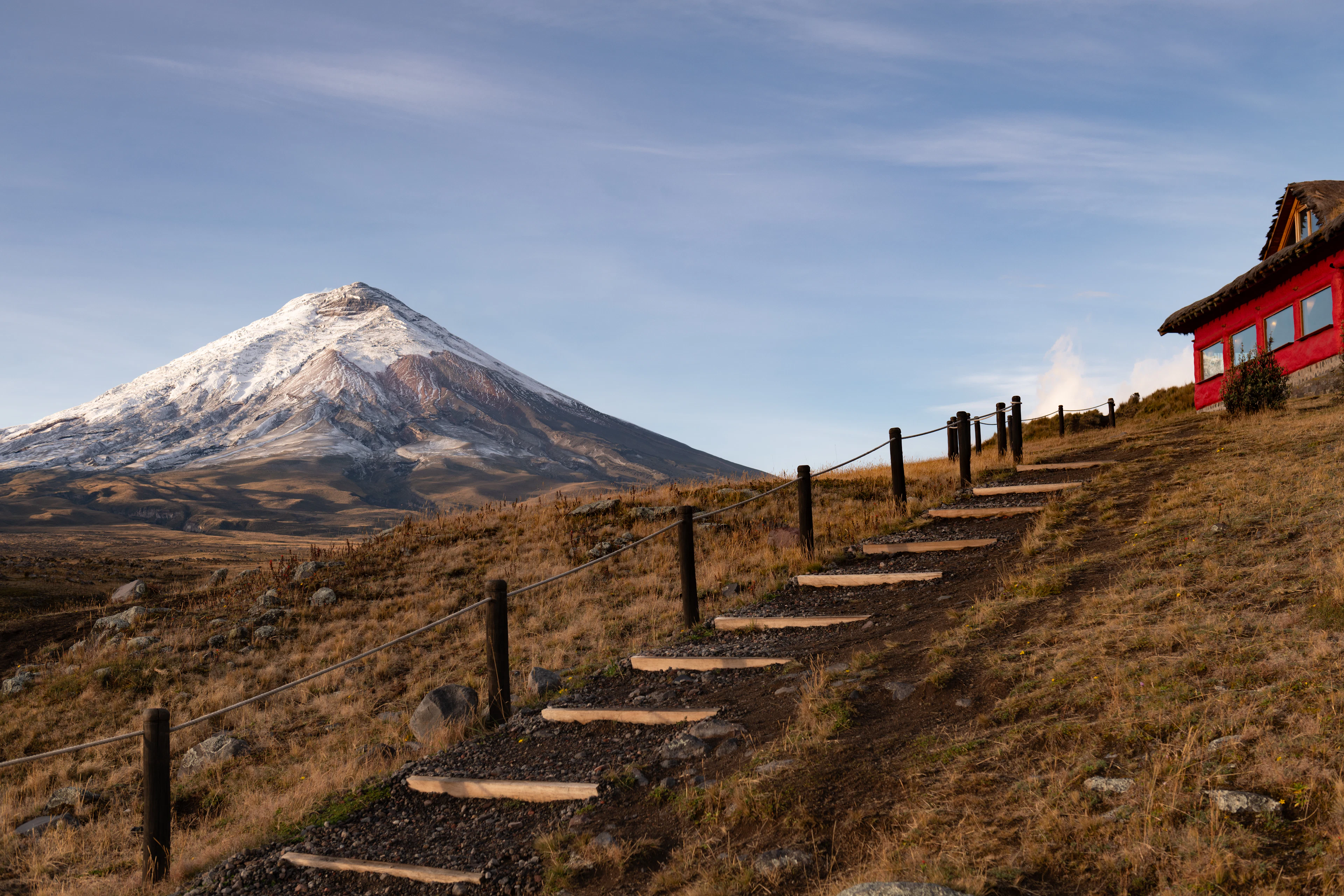 Morning sun on the snow-capped Cotopaxi volcano, with a grassy slope and path in the foreground