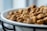 A shallow depth of field captures a close-up view of kibble or dry pet food in a white dish. The focus is on the textured surface of the kibble pieces, with a blurred background.