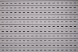 Horizontal metal slats with evenly spaced oblong perforations against a light gray background create a uniform and industrial pattern.