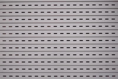 Horizontal metal slats with evenly spaced oblong perforations against a light gray background create a uniform and industrial pattern.