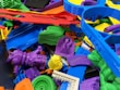 A collection of colorful 3D printed plastic objects in various shapes and colors, piled together. The objects include intricate designs such as gears, abstract forms, and tools, made from materials resembling different parts and components.