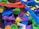 A collection of colorful 3D printed plastic objects in various shapes and colors, piled together. The objects include intricate designs such as gears, abstract forms, and tools, made from materials resembling different parts and components.