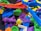 A collection of colorful 3D printed plastic objects in various shapes and colors, piled together. The objects include intricate designs such as gears, abstract forms, and tools, made from materials resembling different parts and components.