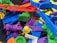 A collection of colorful 3D printed plastic objects in various shapes and colors, piled together. The objects include intricate designs such as gears, abstract forms, and tools, made from materials resembling different parts and components.