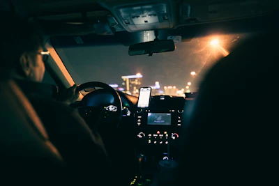 Driver happily using a tablet inside a car with city lights in the background.