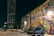 A vibrant street mural reads 'Houston is Inspired' with colorful patterns and shapes surrounding the text. Parked cars, including a blue Chevrolet, are visible in front of the mural. A tall building and street lamps illuminate the scene, creating a lively urban atmosphere at night.