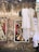 A worn and textured brick wall is adorned with colorful graffiti and torn posters. Elegant, white vintage dresses hang from metal hangers attached to the wall, creating a stark contrast. The scene reflects an intersection of urban decay and retro fashion.