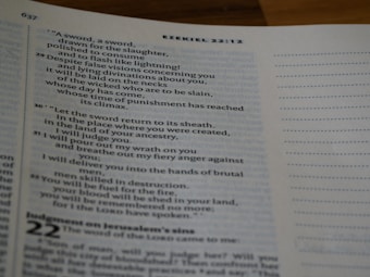 A close-up of an open book displaying text from the book of Ezekiel in the Bible. The text is arranged in verses with chapter and verse numbers visible. The page has a white margin with a light blue tint. The right side of the page features unlined dots for note-taking.