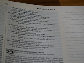 A close-up of an open book displaying text from the book of Ezekiel in the Bible. The text is arranged in verses with chapter and verse numbers visible. The page has a white margin with a light blue tint. The right side of the page features unlined dots for note-taking.