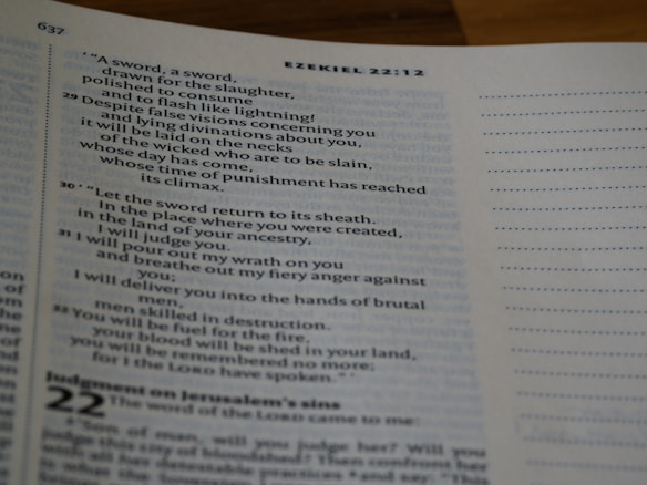 A close-up of an open book displaying text from the book of Ezekiel in the Bible. The text is arranged in verses with chapter and verse numbers visible. The page has a white margin with a light blue tint. The right side of the page features unlined dots for note-taking.