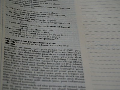 A close-up view of an open page from a book, likely a Bible, featuring printed text with headings and numbered verses. The right-hand side shows a blank lined section.