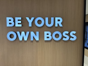 Large white letters spelling 'BE YOUR OWN BOSS' are mounted on a wooden wall, conveying empowerment and independence.