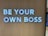 Large white letters spelling 'BE YOUR OWN BOSS' are mounted on a wooden wall, conveying empowerment and independence.