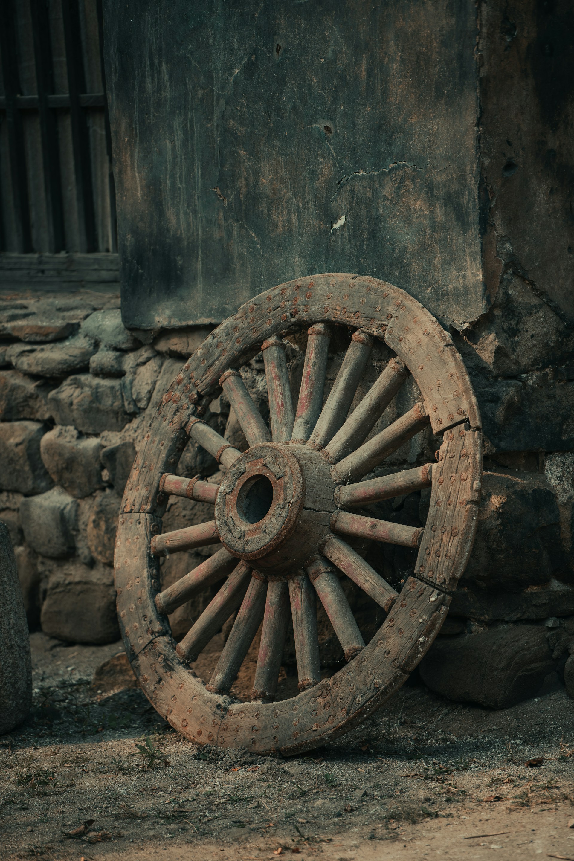 an old wheel leaning against a stone wall