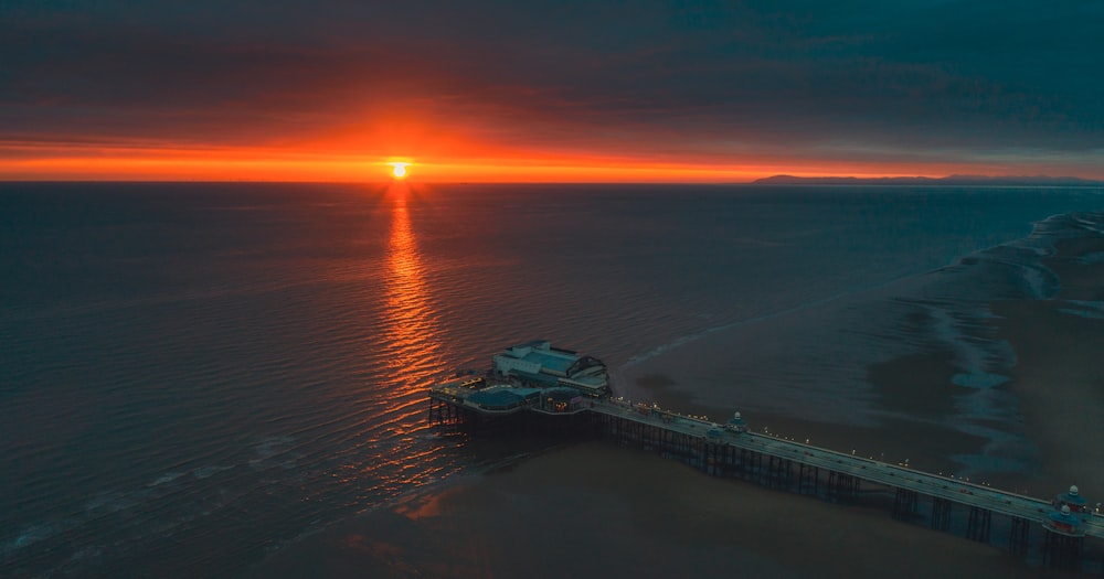 the sun is setting over the ocean and a pier