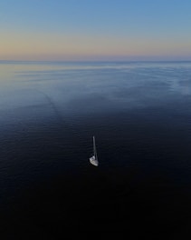 A wide ocean horizon at dawn with a lone sailboat navigating calm waters.