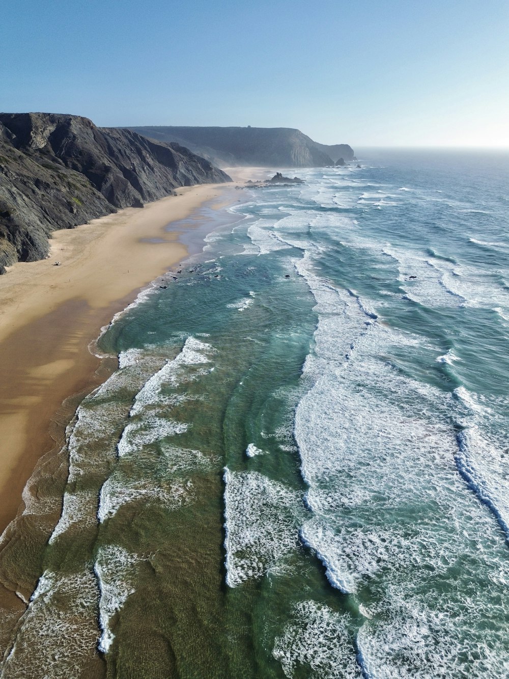 an aerial view of a beach with a cliff in the background