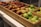 A wooden crate on a table contains various fresh fruits, including apples and plums. The apples are of different varieties, featuring both red and green colors. The fruit is neatly arranged in compartments.