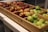 A wooden crate on a table contains various fresh fruits, including apples and plums. The apples are of different varieties, featuring both red and green colors. The fruit is neatly arranged in compartments.