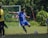 A joyful young soccer player in a blue Arena Latina jersey celebrating a goal on a sunny field.
