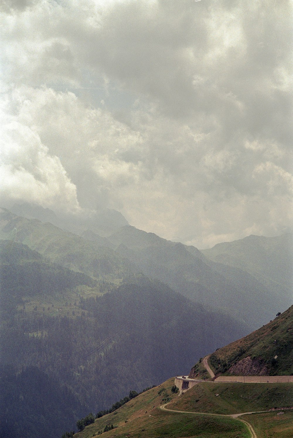 a road winding through a lush green hillside under a cloudy sky